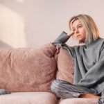 Mulher na casa dos quarenta sentada no sofá, pensativa e cansada, a refletir sobre as mudanças emocionais e energéticas desta fase de transição.