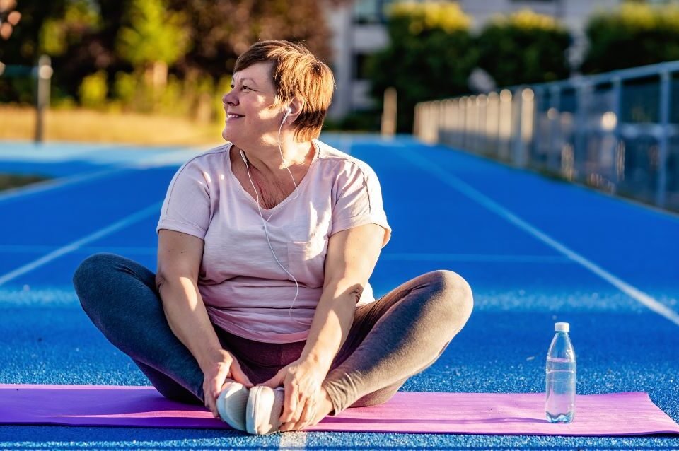 Mulher na menopausa a alongar-se num tapete de yoga ao ar livre, mostrando uma forma natural e energética de aliviar os sintomas.
